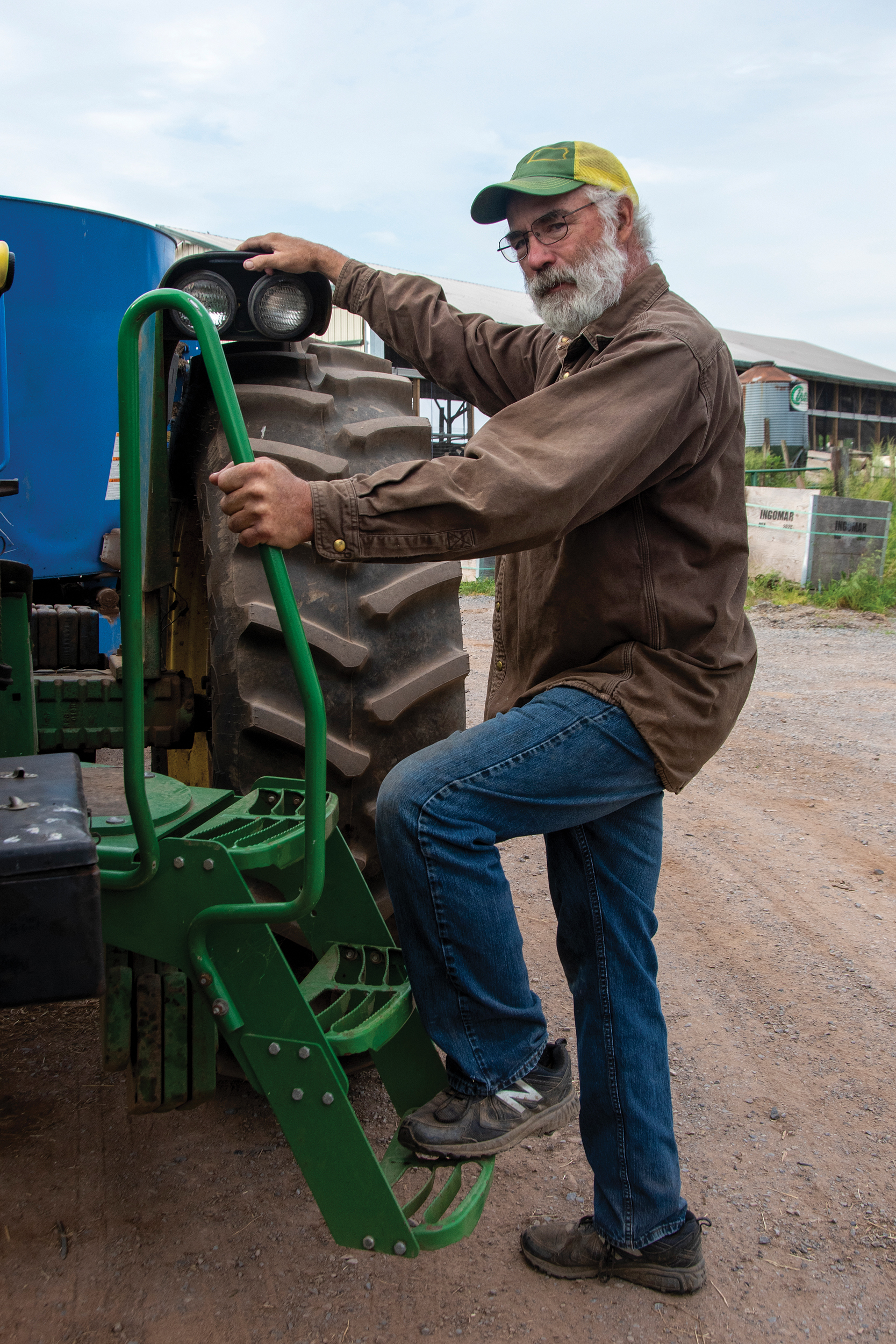 Bob Stanton, co-owner of Manor Meadows Farm in Everett and member of Bedford Rural Electric Cooperative, climbs steps installed on his tractor to ease the burden on his left leg, which has very little muscle tissue left after he suffered a rare disease.